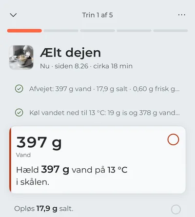 Madlavningstilstanden på første trin, „Ælt dejen“: afvejningen og nedkølingen af vandet er krydset af, og i fokus står vandet, der skal hældes i nu, med grammene i stor skrift.