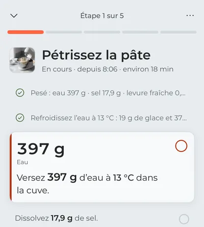 Le mode cuisine à la première étape, « Pétrissez la pâte » : la pesée des ingrédients et le refroidissement de l’eau sont cochés, et l’eau à verser maintenant est au premier plan, ses grammes en gros caractères.