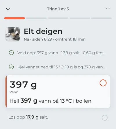Matlagingsmodus på første steg, «Elt deigen»: veiingen og nedkjølingen av vannet er krysset av, og i fokus står vannet som skal helles i nå, med grammene i stor skrift.