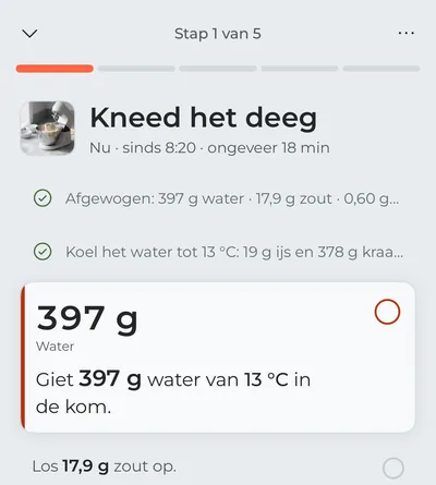 De kookmodus bij de eerste stap, “Kneed het deeg”: het afwegen en het koelen van het water zijn afgevinkt, en in beeld staat het water dat je nu in de kom giet, met de grammen in grote letters.