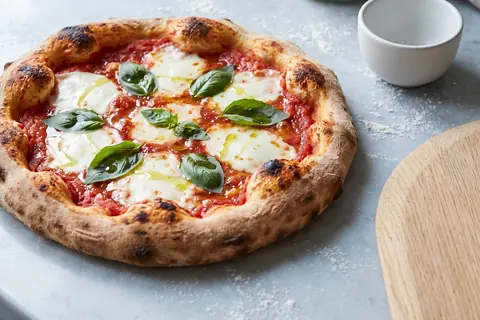 A sourdough Margherita with a darker, blistered rim, and a jar of bubbly starter behind it.