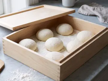 Freshly shaped dough balls, small and smooth, set well apart on flour in a wooden box.