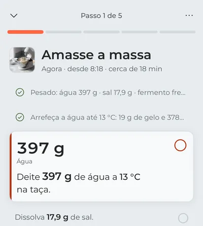 O modo cozinha no primeiro passo, «Amasse a massa»: a pesagem dos ingredientes e o arrefecimento da água já estão marcados, e em destaque está a água a deitar agora, com os gramas em letra grande.