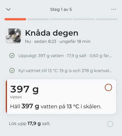 Matlagningsläget på första steget, ”Knåda degen”: uppvägningen och kylningen av vattnet är avbockade, och i fokus står vattnet som ska hällas i nu, med grammen i stor stil.